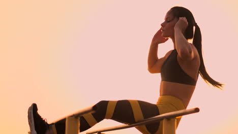 Candid-shot-of-real-healthy-and-fit-woman-performing-hanging-leg-raises-on-outdoor-fitness-station-in-sunset-at-beach-promenade.-Showing-strong-abdominal-six-pack.